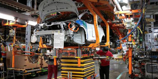 Focused auto mechanic working on a car production line with unfinished cars in a row at automobile sector.